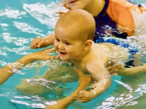 Baby smiling in the water whilst being held by teacher