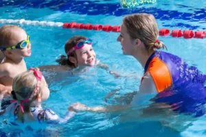 Swim teacher talking to three students in the pool