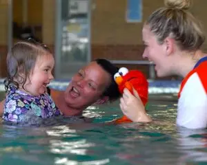 Mum, baby and teacher in the water playing together
