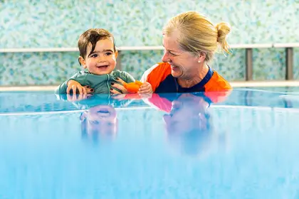 Swim teacher sitting in the water with a baby