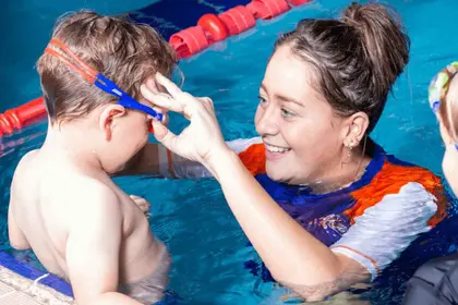 A swim teacher helping a student put on their goggles