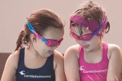 Two young girls smiling at eachother poolside