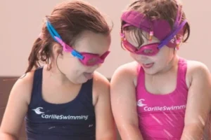 Two young girls sitting by the pool in Carlile Swim bathers