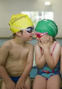Two students sitting on the side of the pool