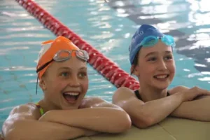 Two young girls holding onto the side of the pool