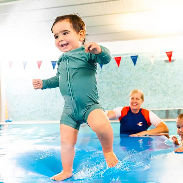 Swim teacher supports a parent and baby in an indoor pool during a WaterBabies lesson, practising gentle water familiarisation and early confidence skills.