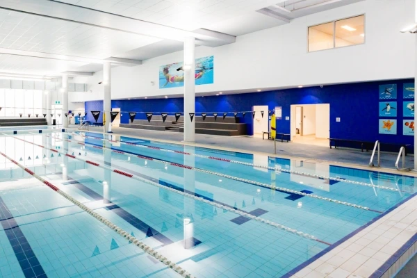 Indoor heated lap pool at Carlile Swim Warriewood, showing multiple lane ropes, tiled pool deck, and the bright indoor facility.