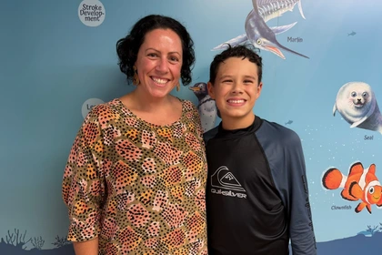 Zachary and his mum standing in front of the steps to success sign at Carlile Swim