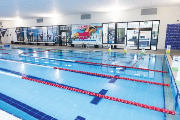 Indoor lap pool at Carlile Swim Arana Hills, showing marked swim lanes with lane ropes, tiled pool deck, and the heated indoor facility.