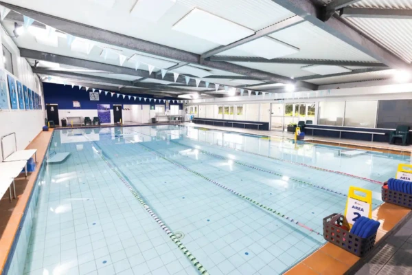 Indoor heated lap pool at Carlile Swim Aspley, showing marked lanes with lane ropes, tiled pool deck, and the bright indoor swim centre.
