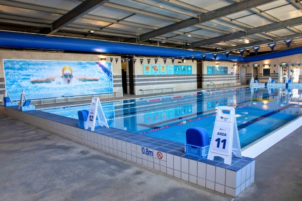 Indoor heated lap pool at Carlile Swim Ferntree Gully, showing marked lanes with lane ropes, tiled pool deck, and the indoor swim centre.